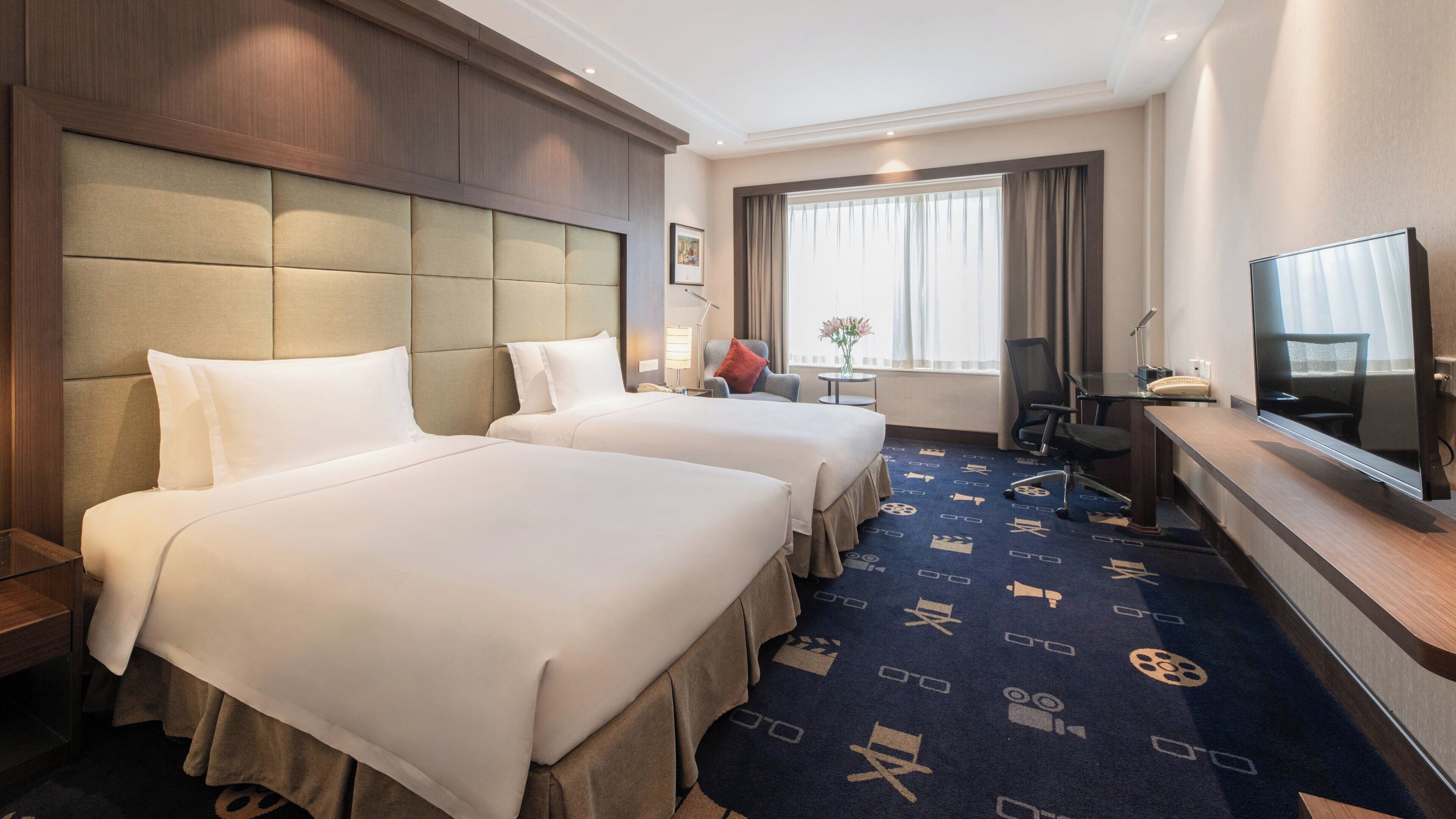 A hotel room with two beds, a desk with a television, and a window with curtains.