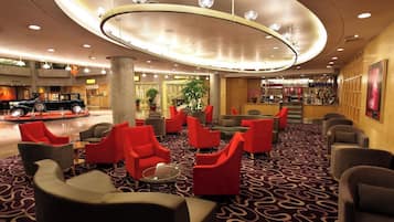 A hotel lobby with a circular ceiling light fixture, red and grey seating, and a bar area.