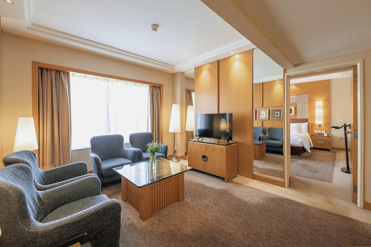 A hotel room with a seating area, a television, a mirror, and a bed.