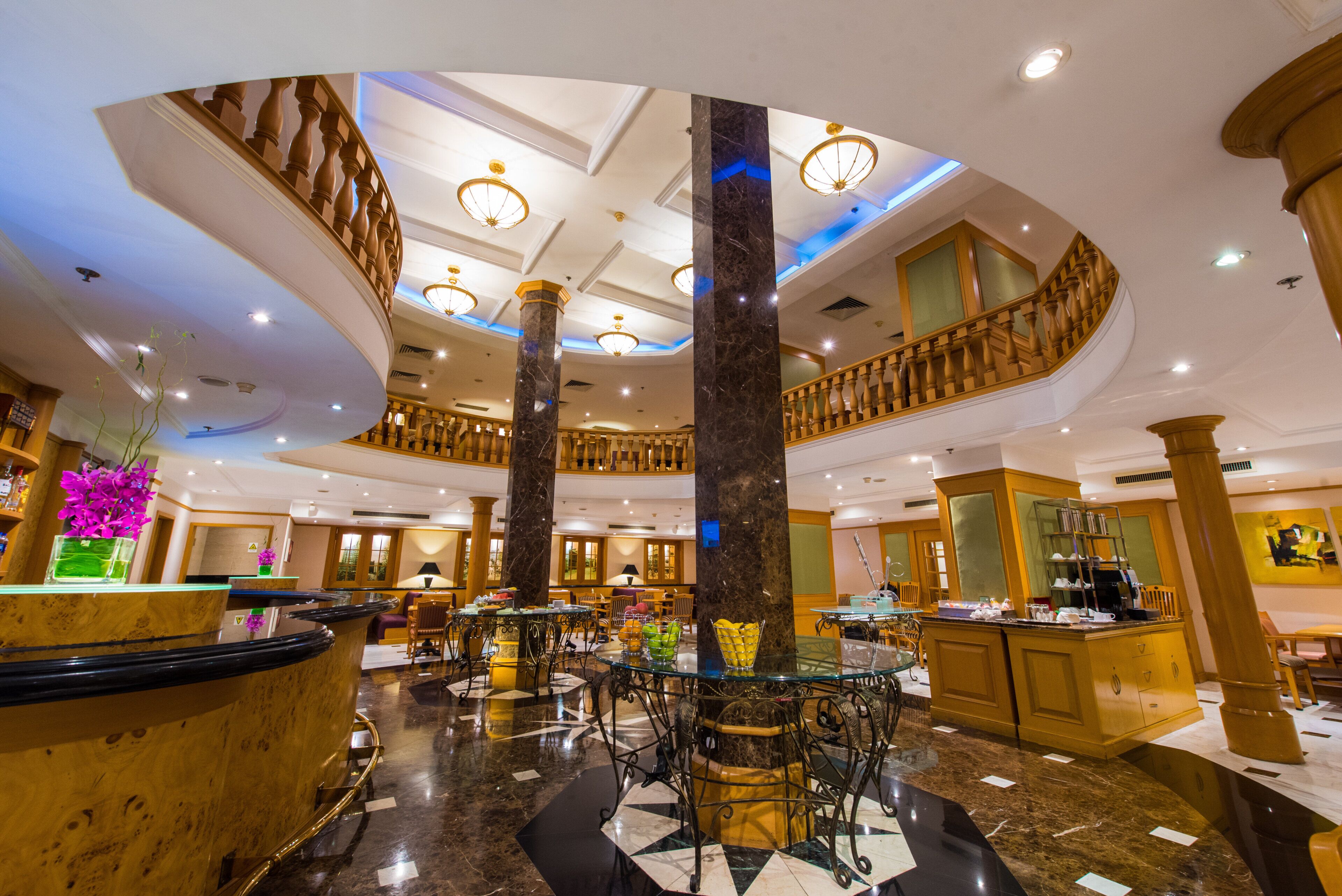 A hotel lobby with a grand staircase, marble columns, and a reception desk.