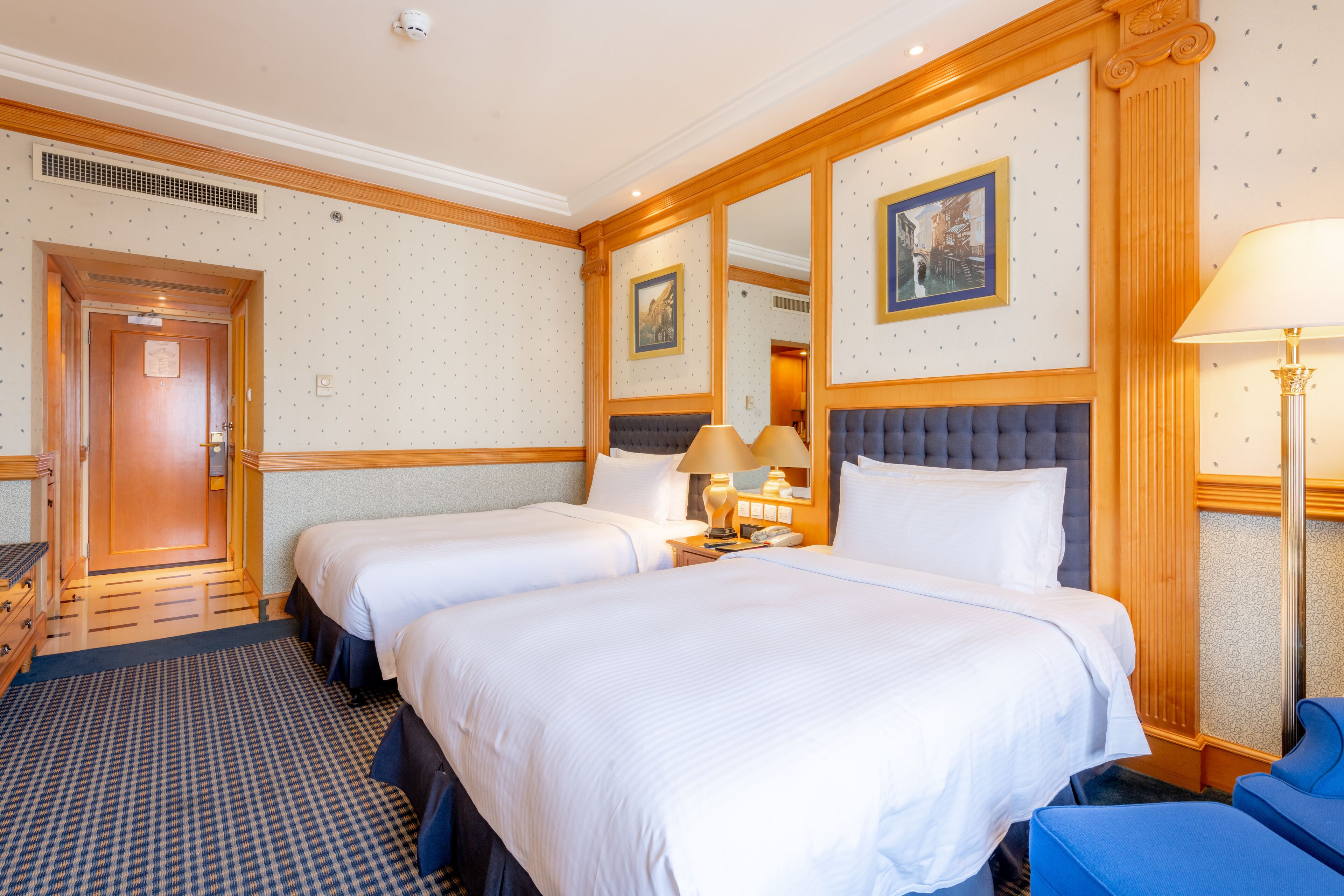 Ein Hotelzimmer mit zwei Betten, einem großen Spiegel und einem blauen Sessel.