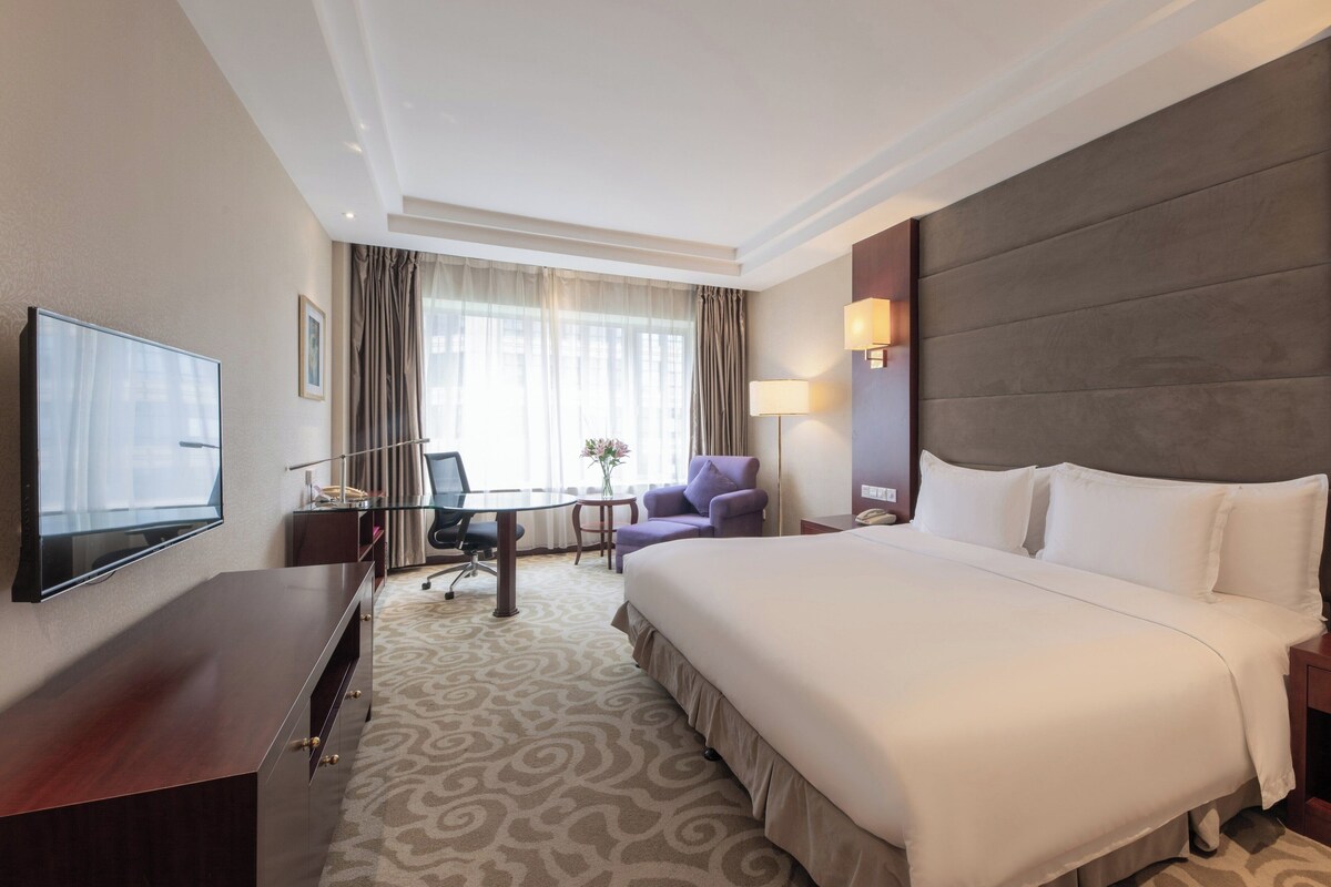 Una habitación de hotel con una cama grande, un escritorio con una silla, un televisor y una ventana con cortinas.