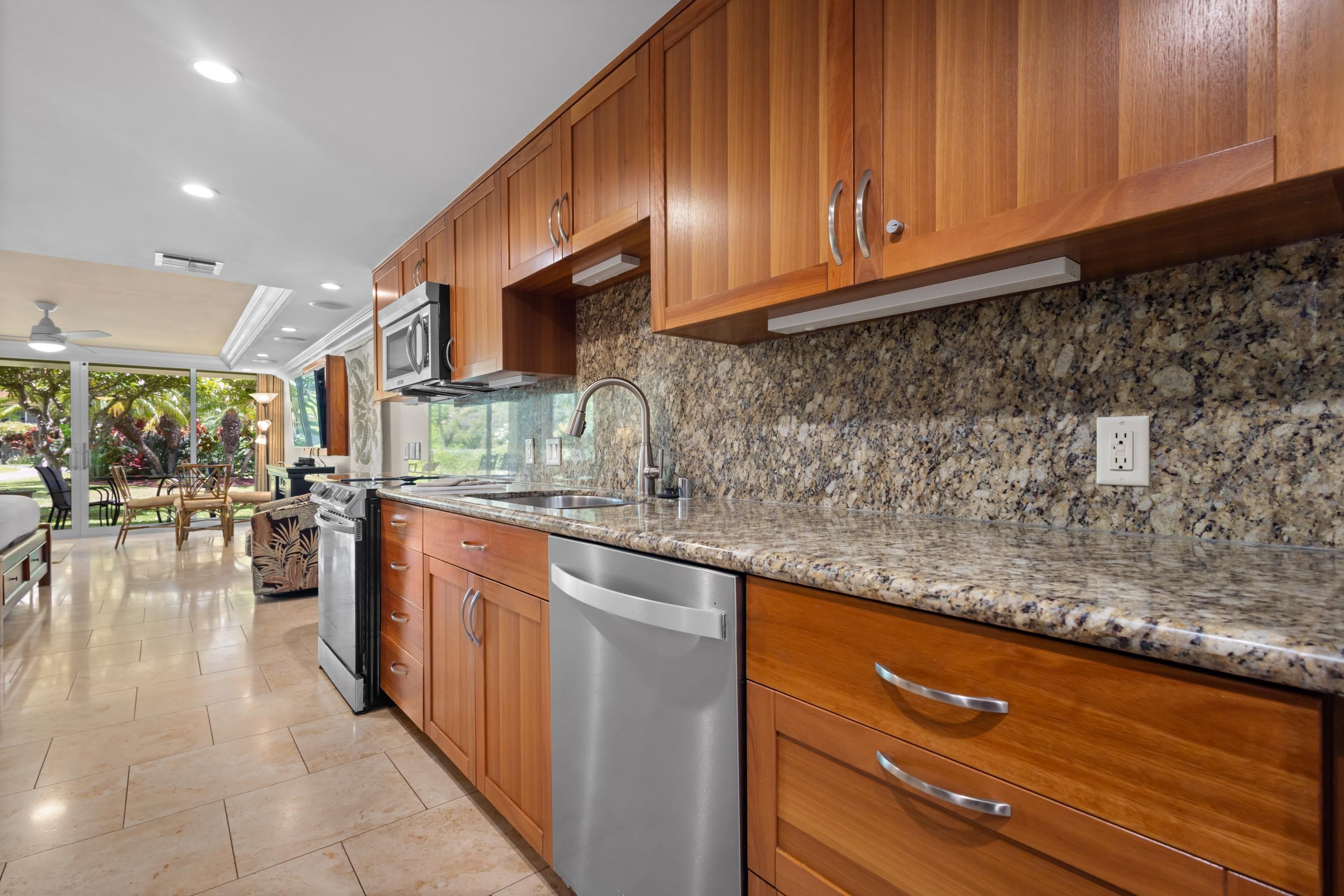 A kitchen with wooden cabinets, a granite countertop, stainless steel appliances, and a view of the outdoors.