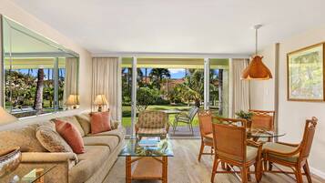 A spacious living area with a glass coffee table, a sofa, and wicker chairs.