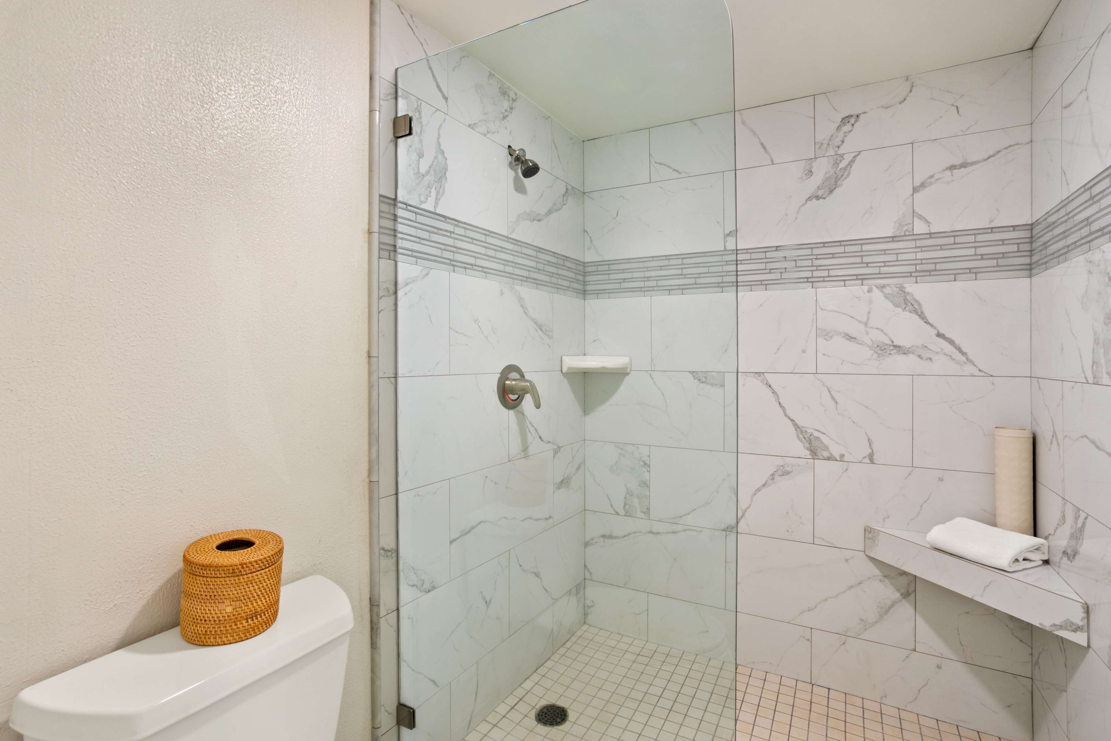 A shower with glass doors, a toilet with a toilet paper holder, and a towel rack.