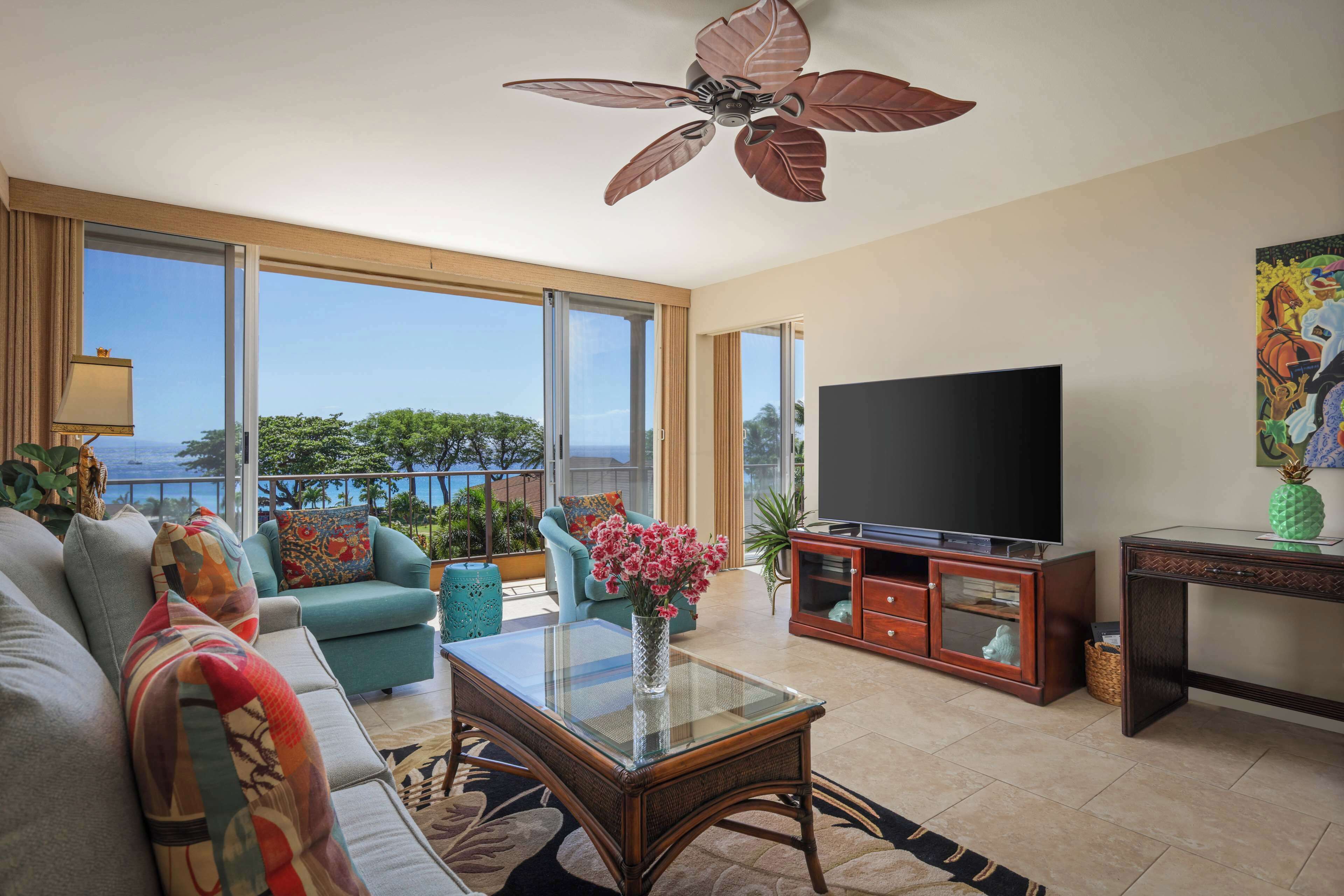 A spacious living room with a large TV, comfortable seating, a ceiling fan, and a view of the outdoors.