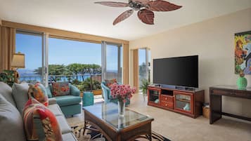 A spacious living room with a large TV, comfortable seating, a ceiling fan, and a view of the outdoors.