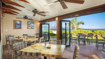 An outdoor patio with tables and chairs, ceiling fans, and a view of the ocean.