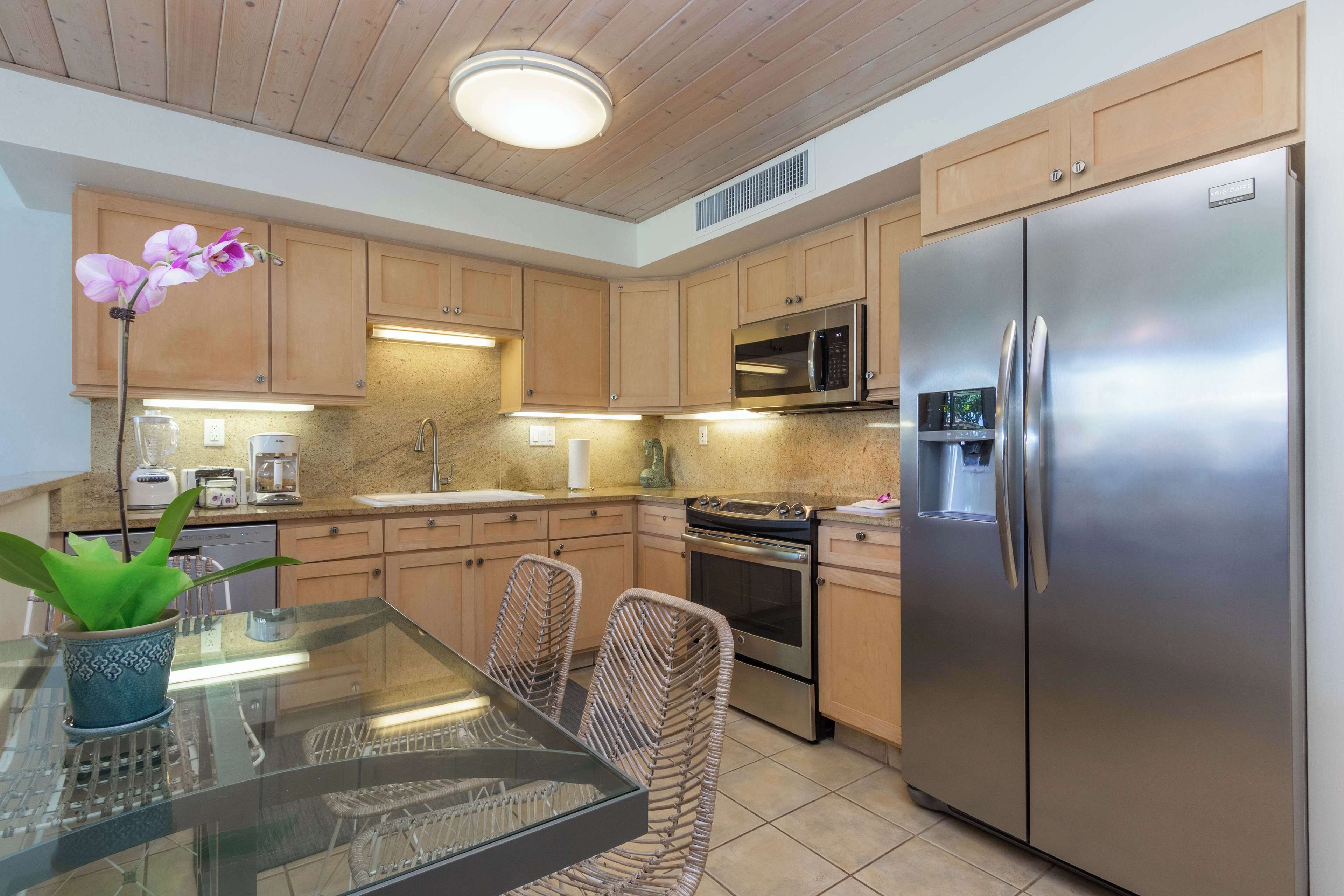 A modern kitchen with wooden cabinets, stainless steel appliances, a glass dining table, and wicker chairs.