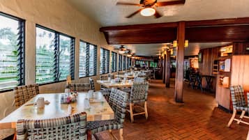 A restaurant with multiple tables and chairs, large windows, and a herringbone floor pattern.