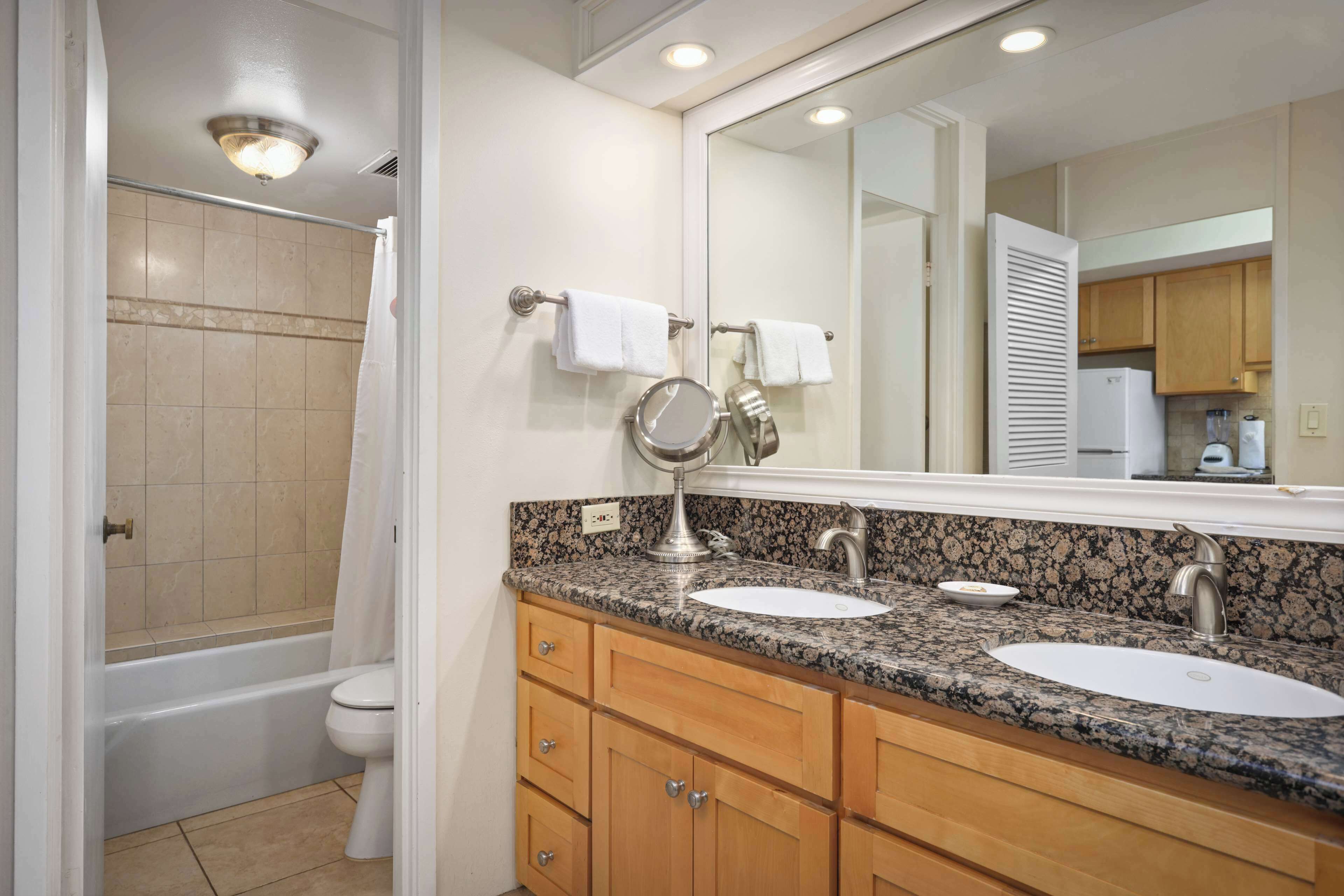 A bathroom with a bathtub, two sinks, a mirror, and wooden cabinets.