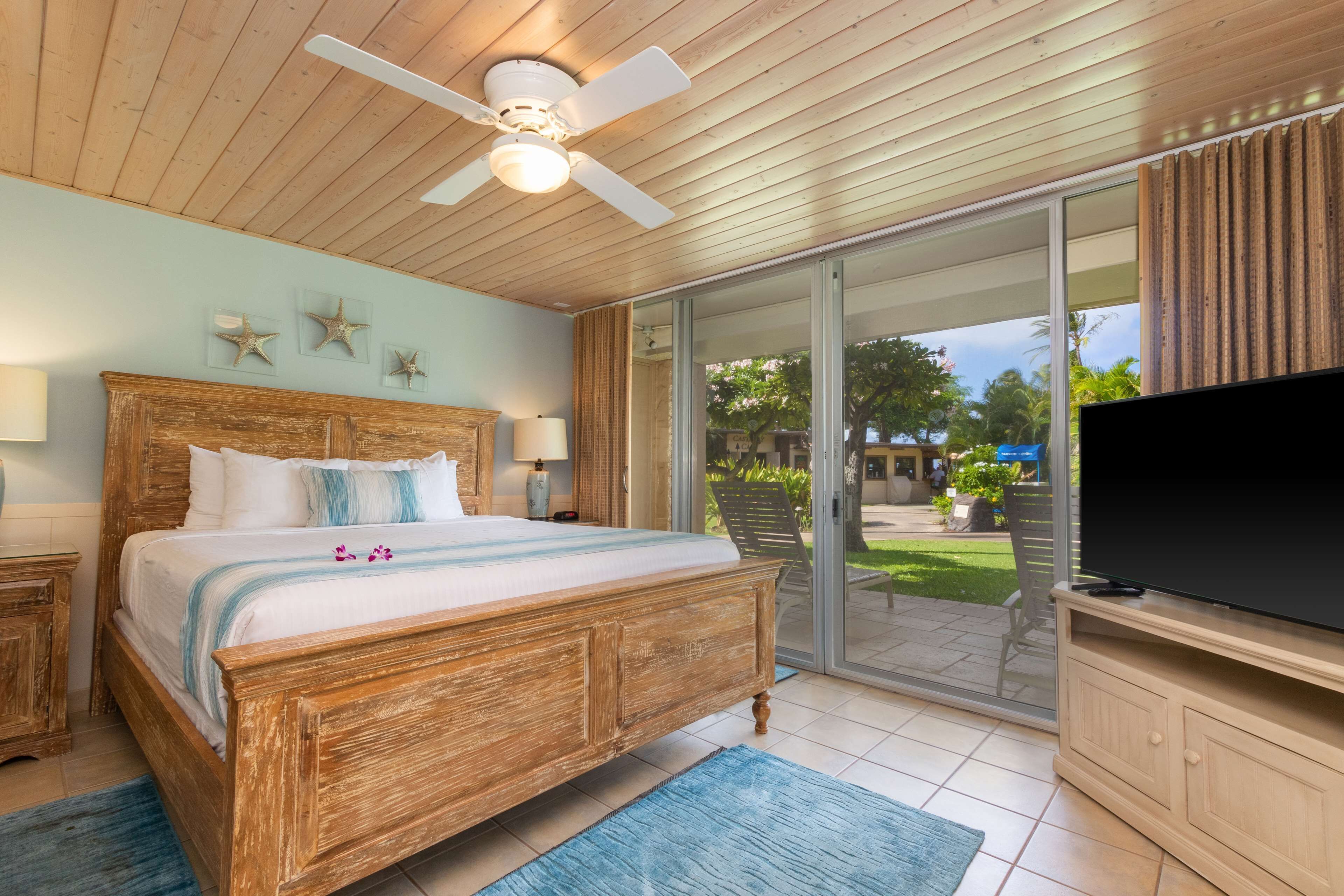 Een slaapkamer met een houten bed, een plafondventilator, een televisie en een schuifdeur naar een terras.