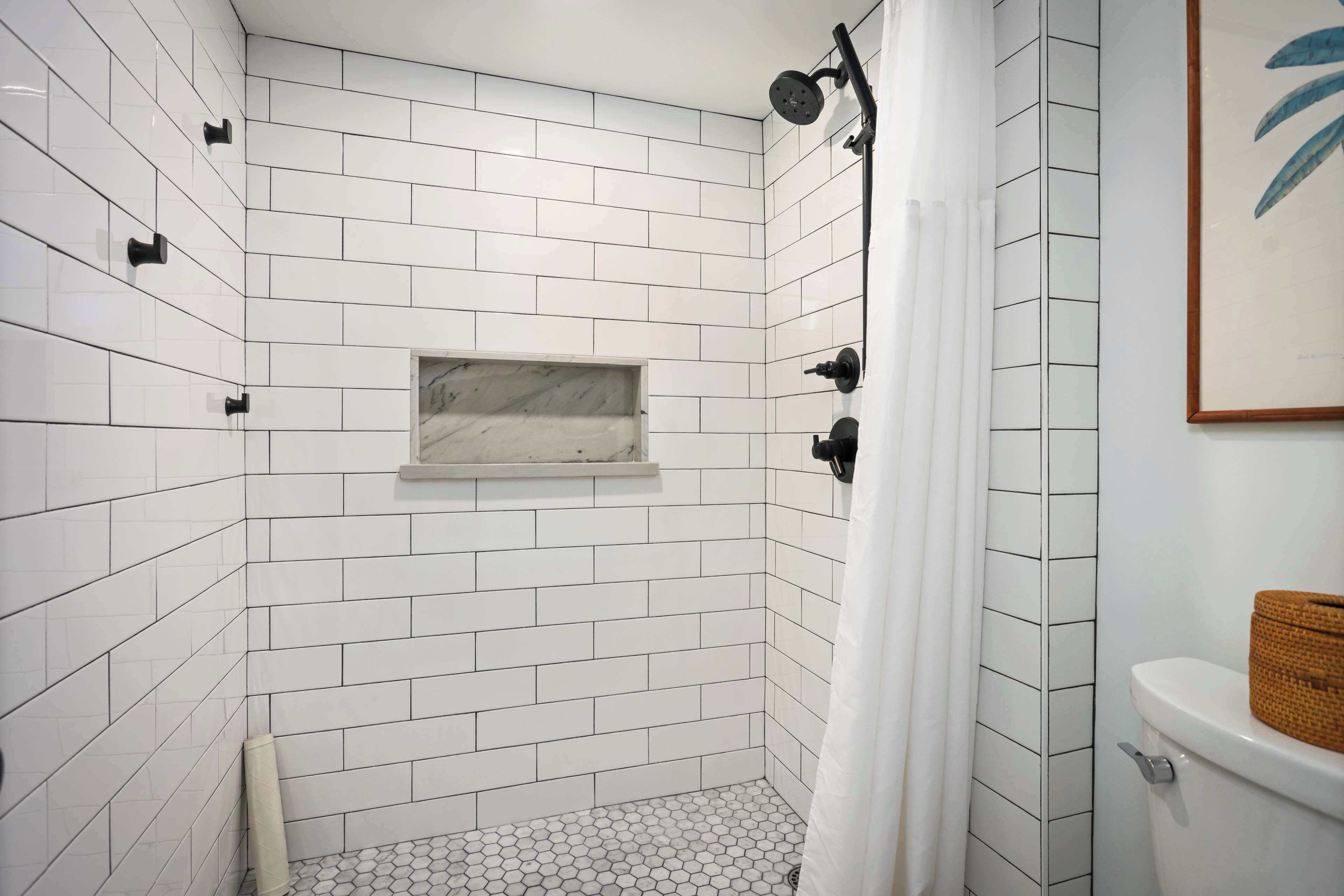 Ducha con azulejos blancos, repisa de mármol y un inodoro con una cesta.