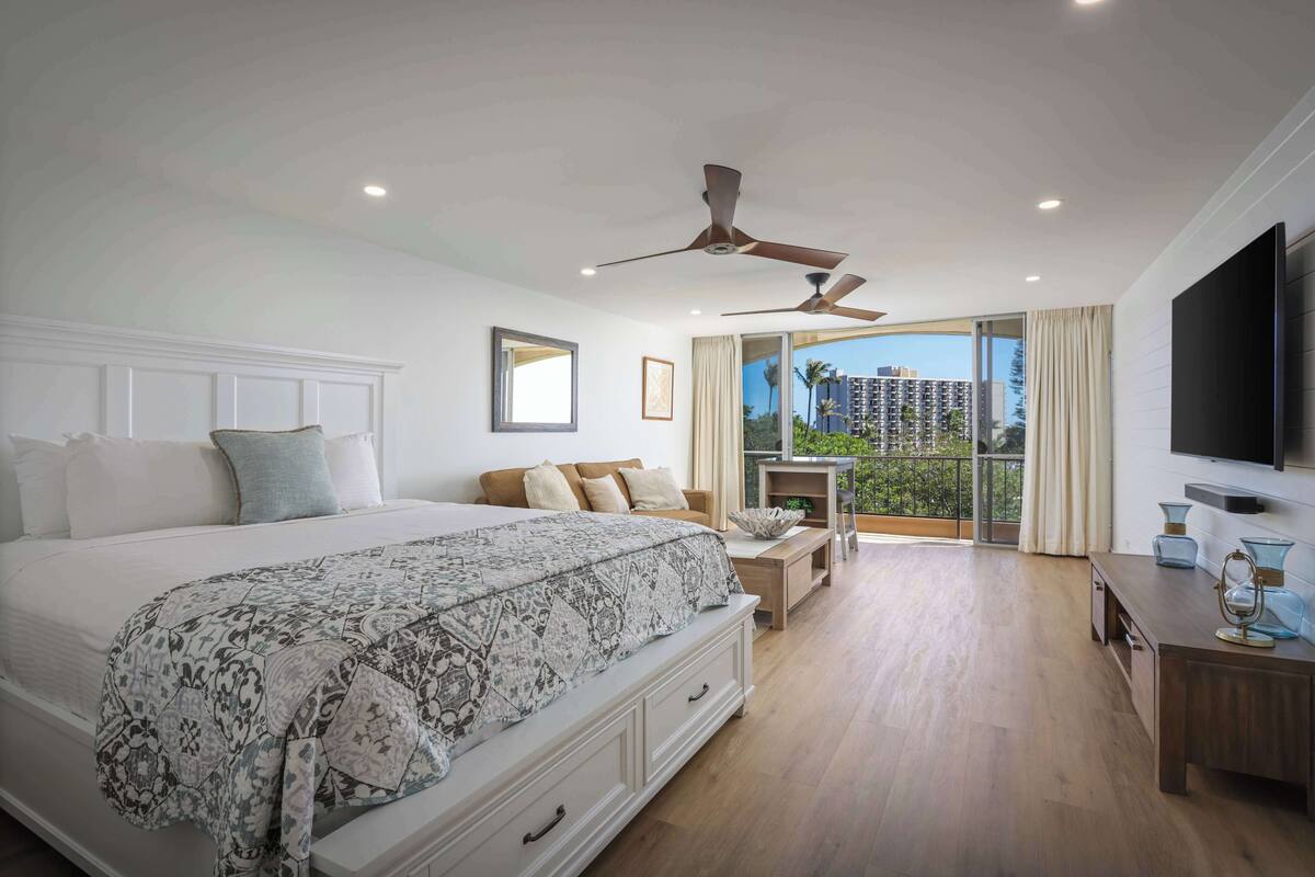 Ein Schlafzimmer mit einem großen Bett, Deckenventilatoren, einem Fernseher und einem Balkon mit Blick.