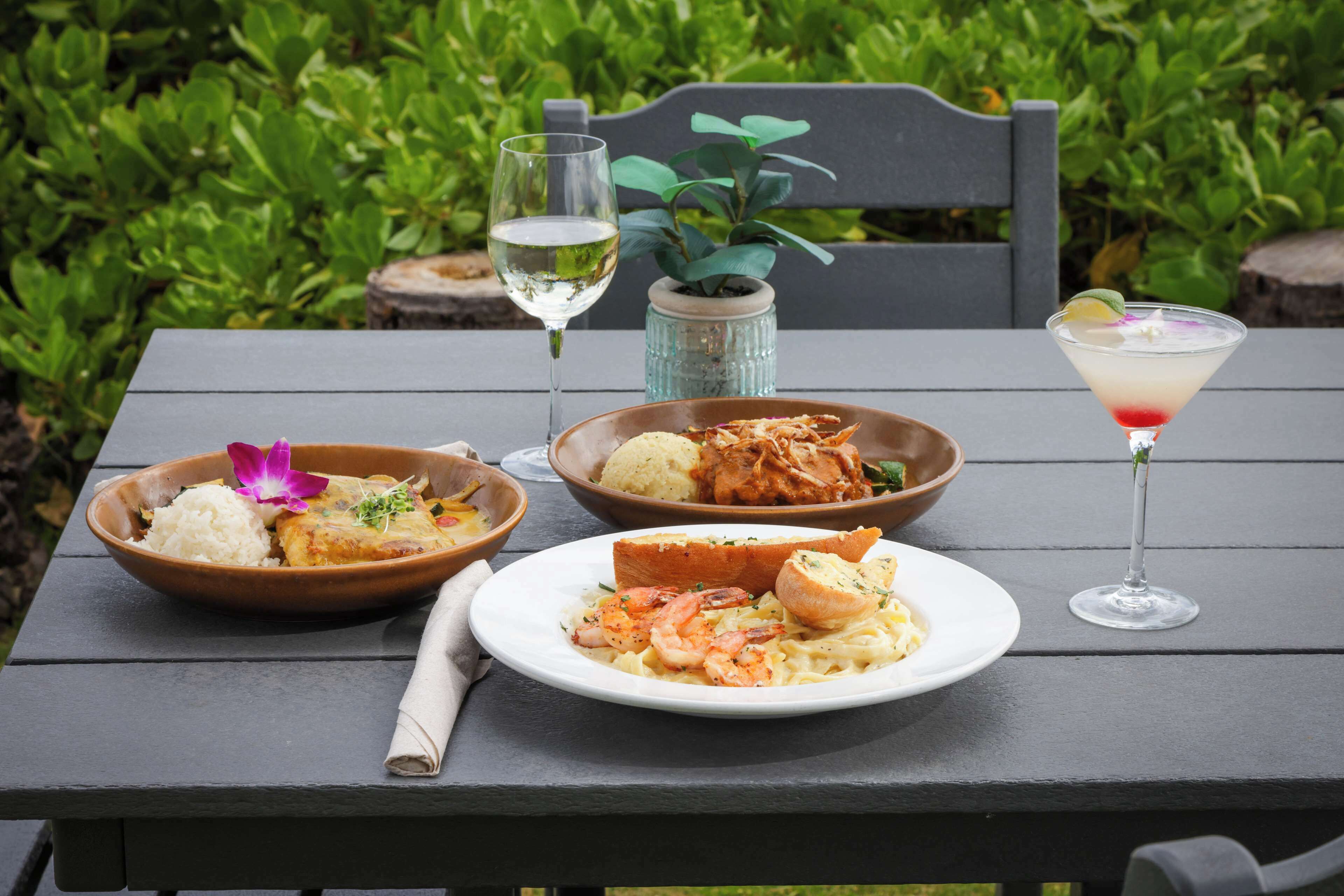 A table with a meal and two drinks, surrounded by greenery.