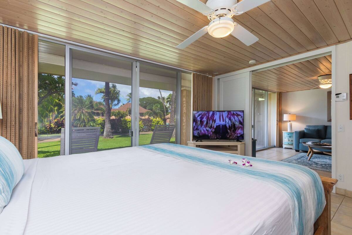 Ein Schlafzimmer mit einem großen Bett, einem Fernseher und einer Glasschiebetür, die auf einen Balkon führt.