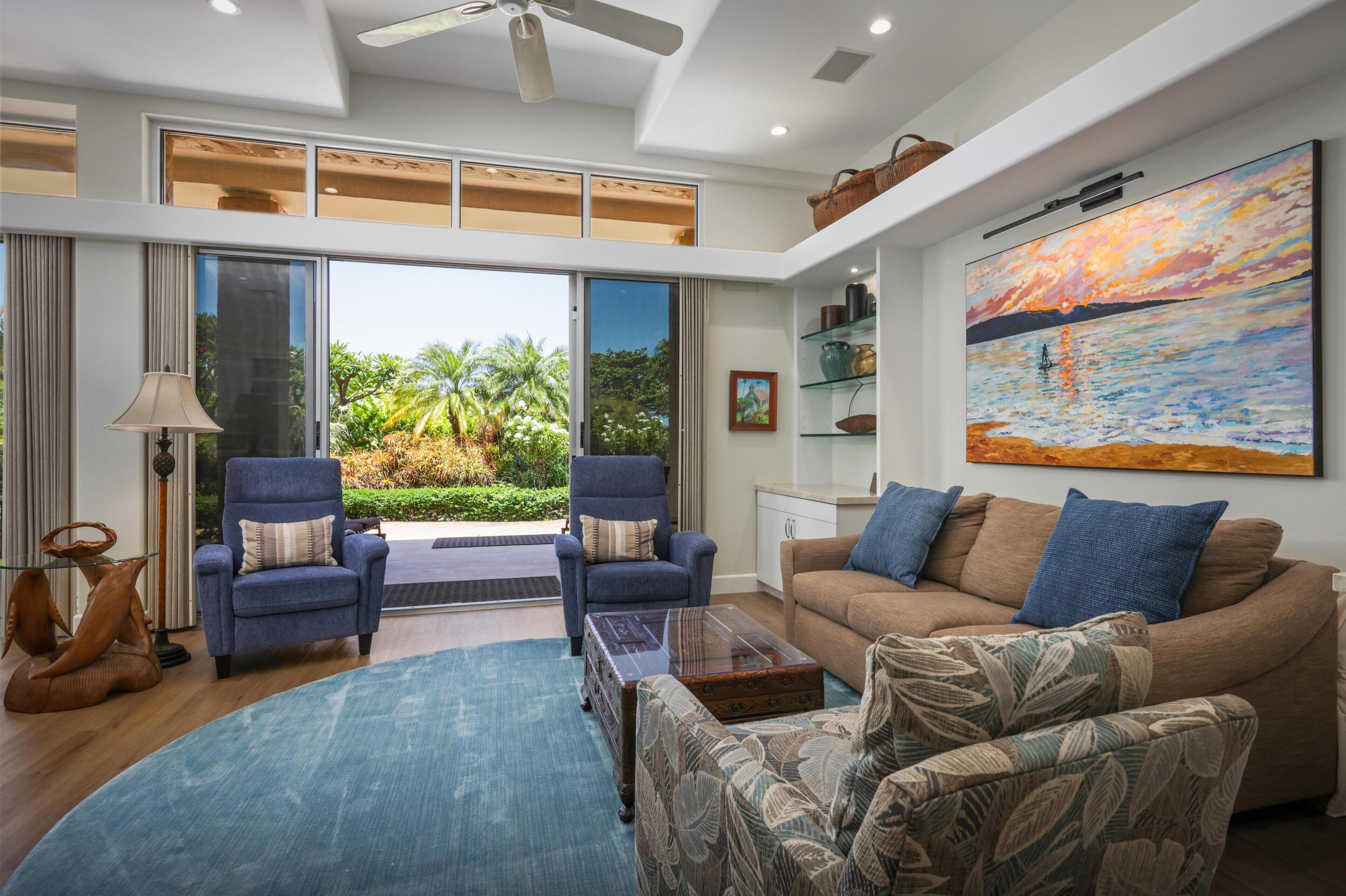A spacious living room with a large window, a ceiling fan, and a painting on the wall.