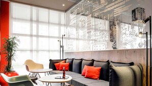 Un'area lounge moderna con divano, poltrone, un tavolo, una pianta e un muro con decorazioni artistiche.