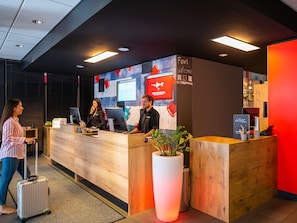A reception desk with a 'Feel Welcome' sign, a digital screen, and a large potted plant. - ibis Muenchen City (Munich)