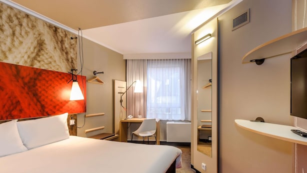 Une chambre d’hôtel avec un lit, un bureau, une chaise, une télévision et un miroir.