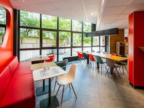 A modern restaurant with large windows, red seating, and a variety of chairs. - ibis Muenchen City (Munich)