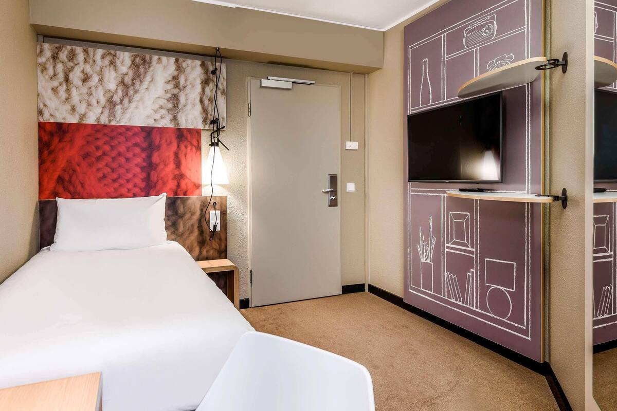A hotel room with a bed, a TV, a desk, and a wardrobe with chalkboard designs.