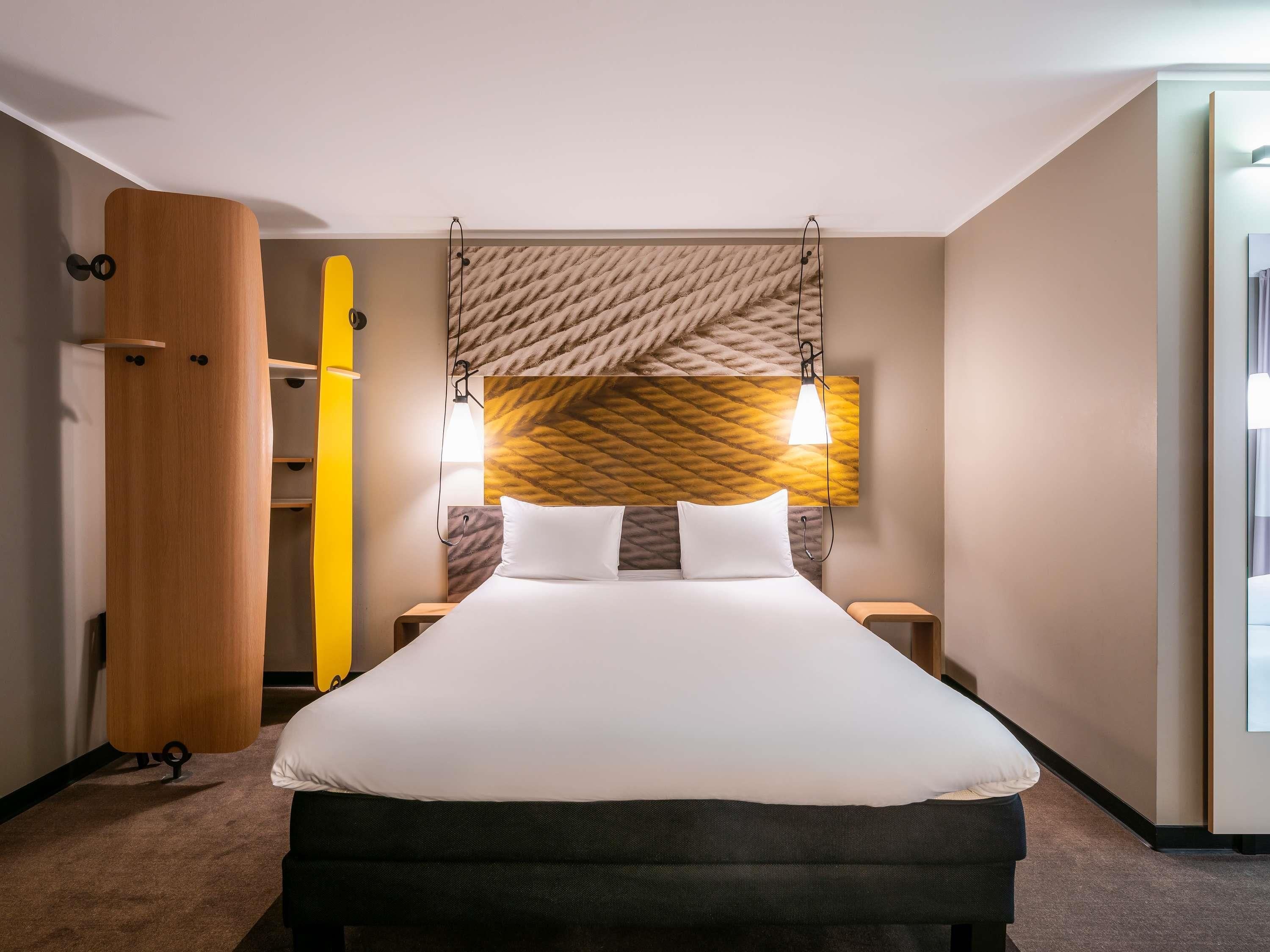 A hotel room with a large bed, a wooden wardrobe, and a headboard with a geometric pattern.