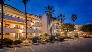 A multi-story hotel with balconies, a parking lot, and palm trees.