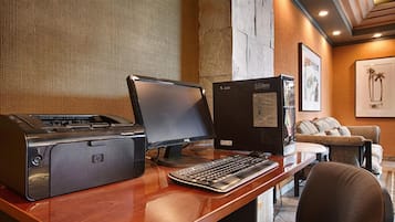 Angolo studio in hotel con stampante HP, monitor Dell e tastiera su una scrivania in legno.