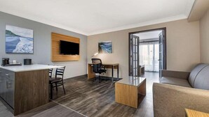 A modern hotel room with a wooden desk, a comfortable sofa, a flat-screen TV mounted on the wall, and artwork on the walls.