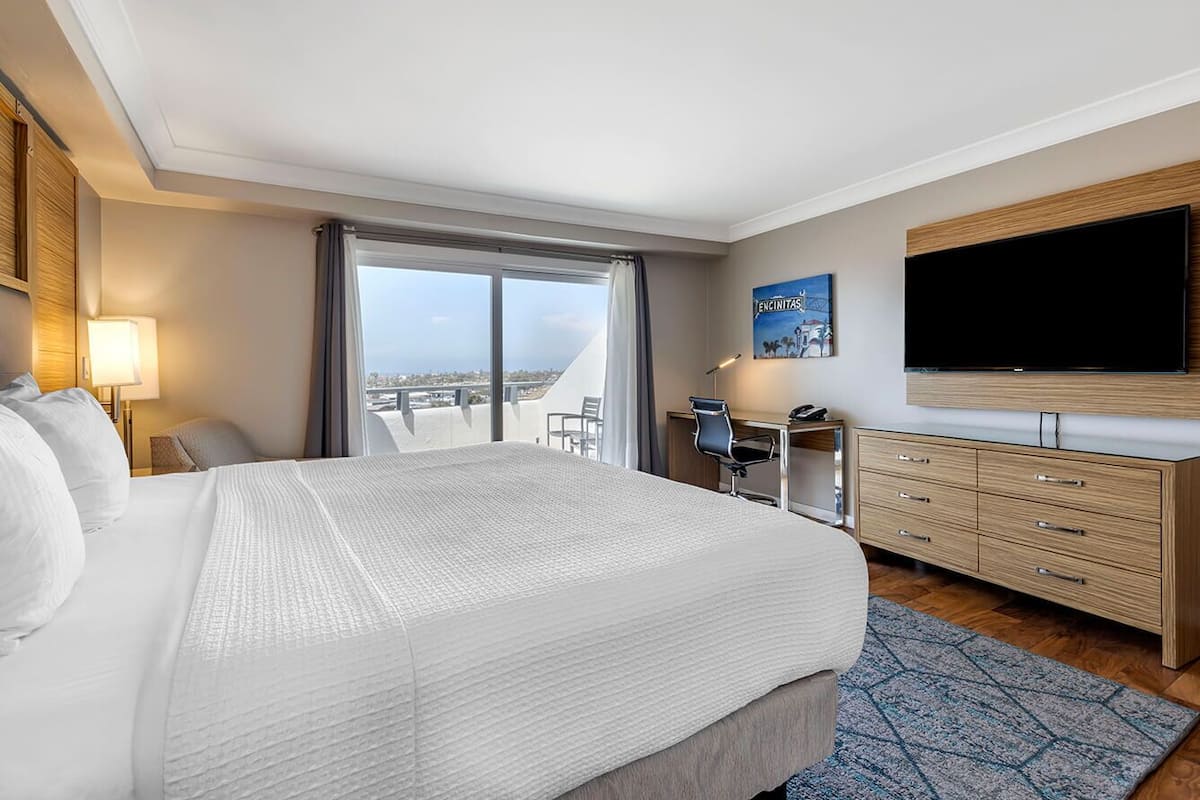 Quarto de hotel com uma cama grande, uma escrivaninha, uma cadeira, uma televisão e vista para a cidade.