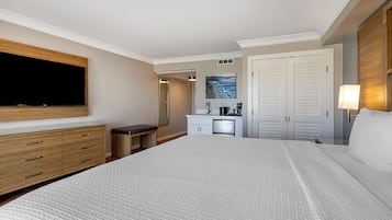 A hotel room with a large bed, a TV mounted on the wall, a desk with a chair, a painting on the wall, and a wardrobe.