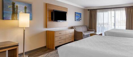 Una habitación de hotel con cama, escritorio, televisor montado en la pared, cómoda y ventana con cortinas.