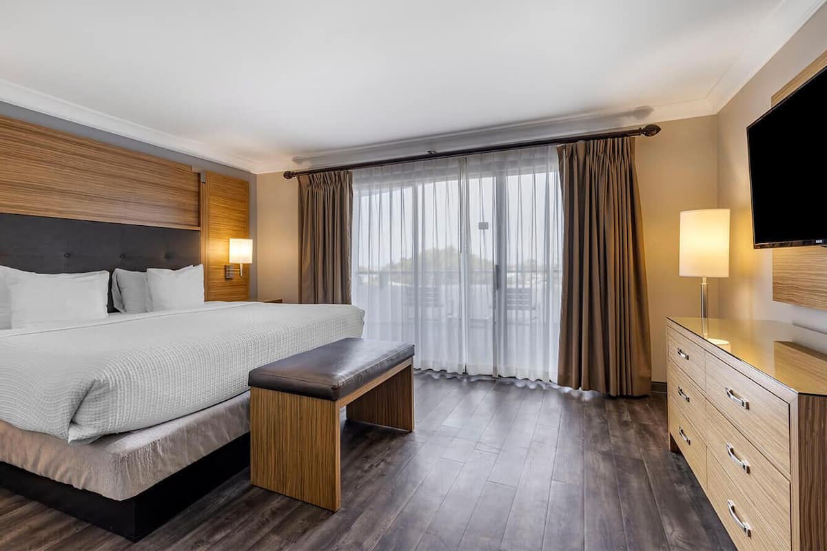 Quarto de hotel com uma cama grande, um banco, uma televisão e uma cômoda.