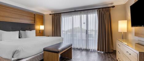 A hotel room with a large bed, a bench, a TV, and a dresser.