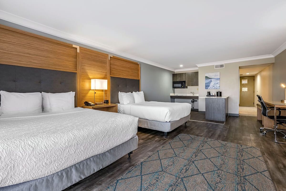 Quarto de hotel com duas camas, uma cozinha compacta, uma escrivaninha e um banheiro.