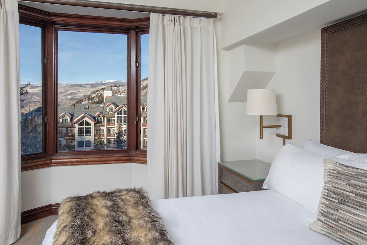 A hotel room with a large window offering a view of a mountainous landscape.
