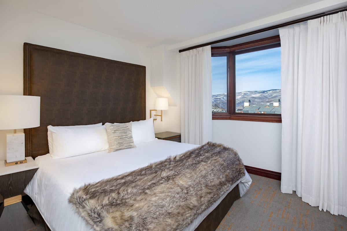 A hotel room with a large bed, a view of the mountains through a window, and a fur throw on the bed.