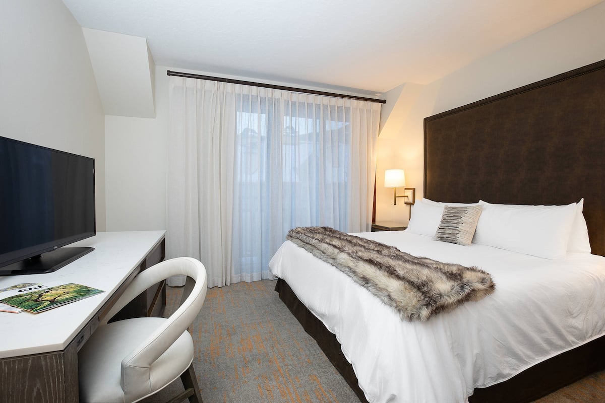 A hotel room with a bed, a desk with a computer, a chair, and a window with curtains.