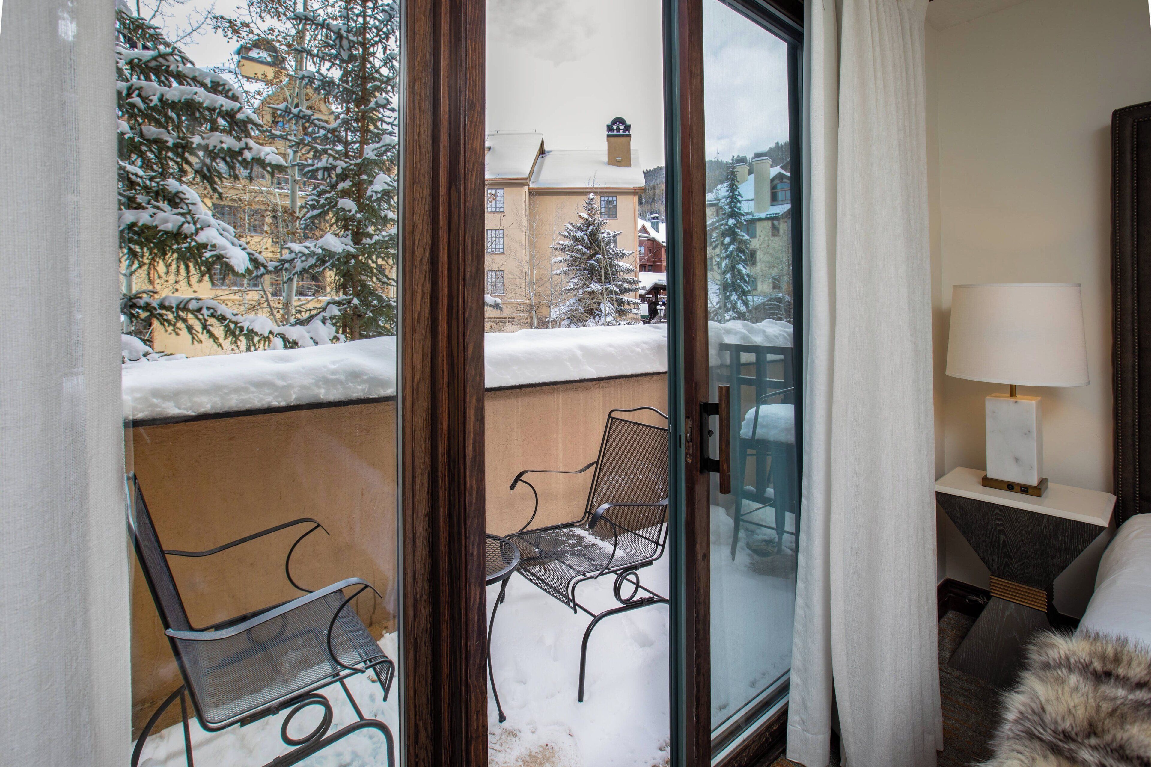Ein Zimmer mit Blick auf eine verschneite Landschaft, eine Glastür, ein Sessel, ein Tisch und eine Lampe.