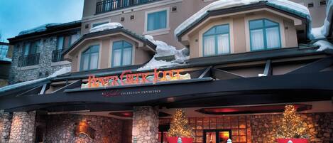 A hotel with a stone facade, a large Christmas tree, and snow on the roof.