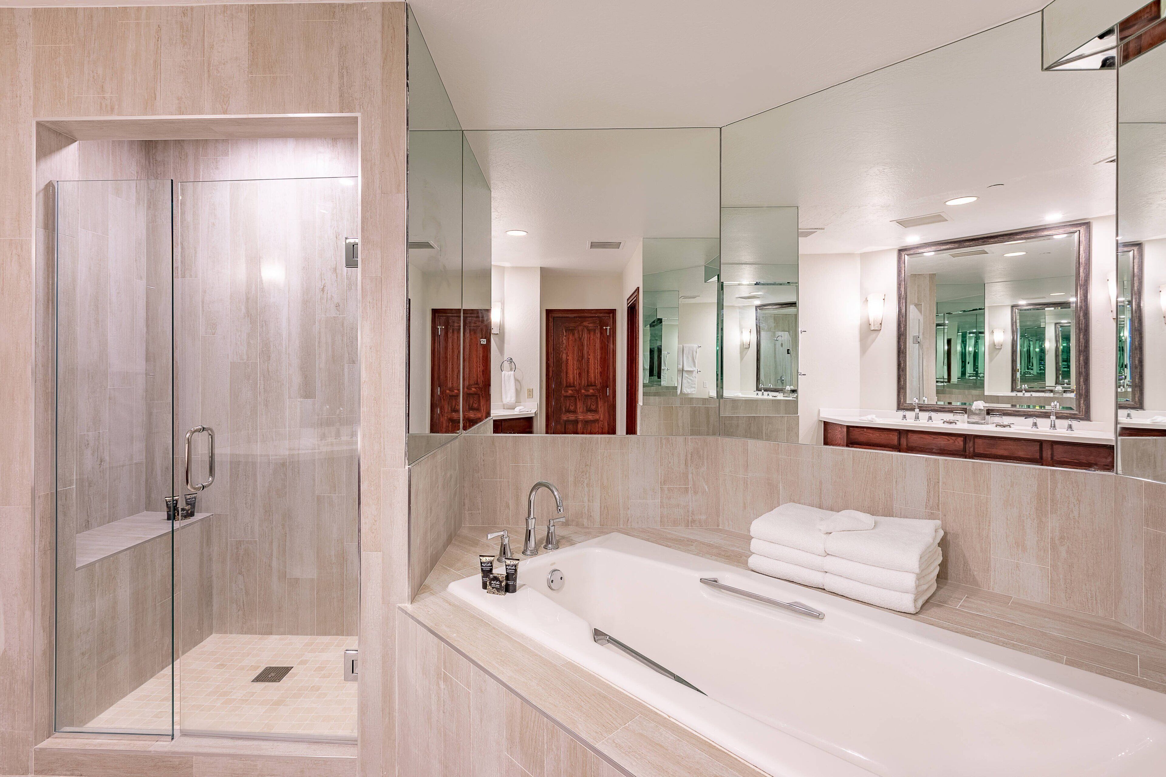 Un baño moderno con ducha envuelta en vidrio, una bañera grande y un lavamanos con espejo.