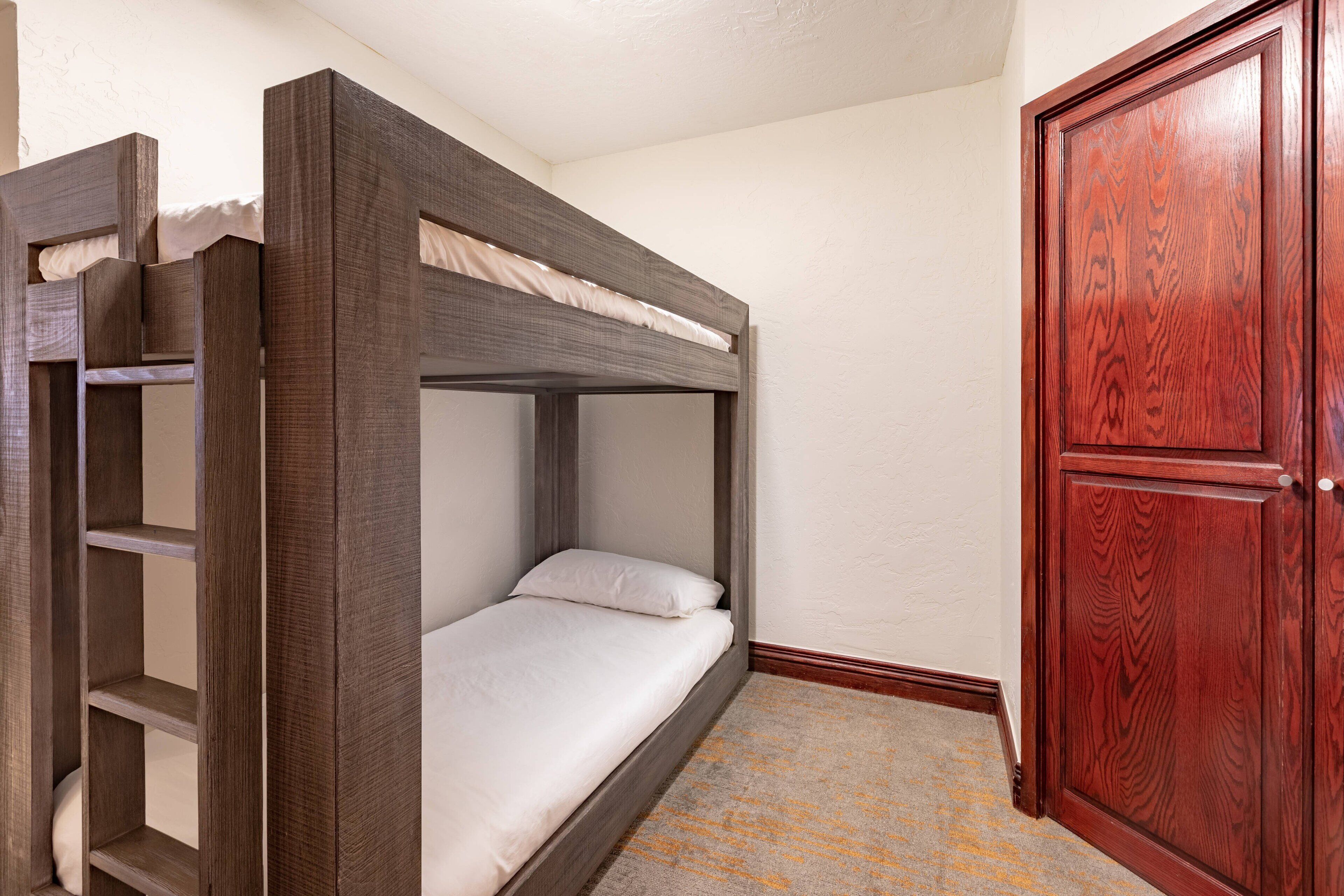 A bunk bed with a wooden frame and white bedding, a wooden door, and a carpeted floor.