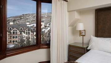 A hotel room with a large window, a bed, a bedside table with a lamp, and a view of a snowy landscape.