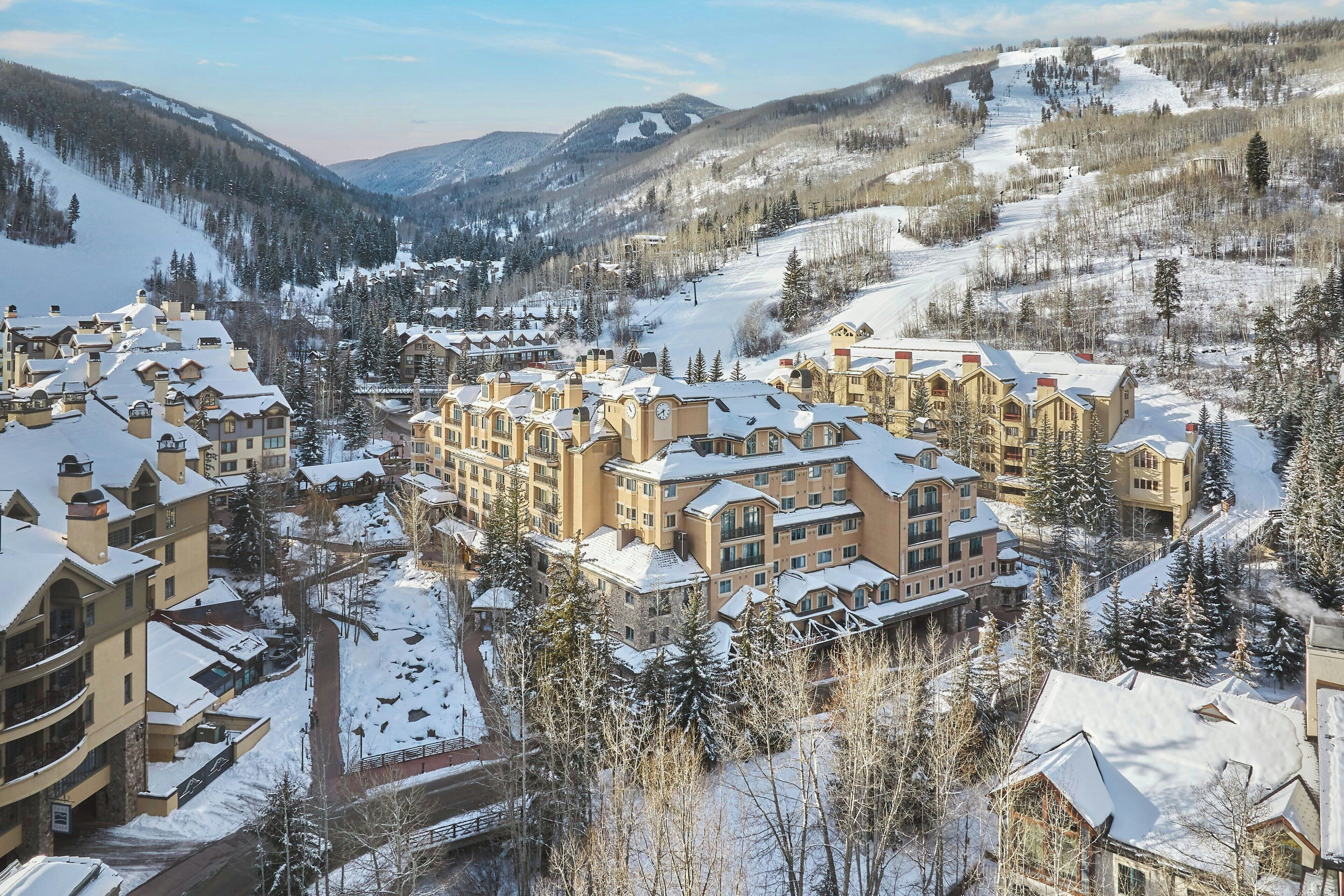 Ein schneebedecktes Resort mit mehreren Gebäuden, darunter ein großes Hotel mit Innenhof und umliegenden kleineren Bauten.