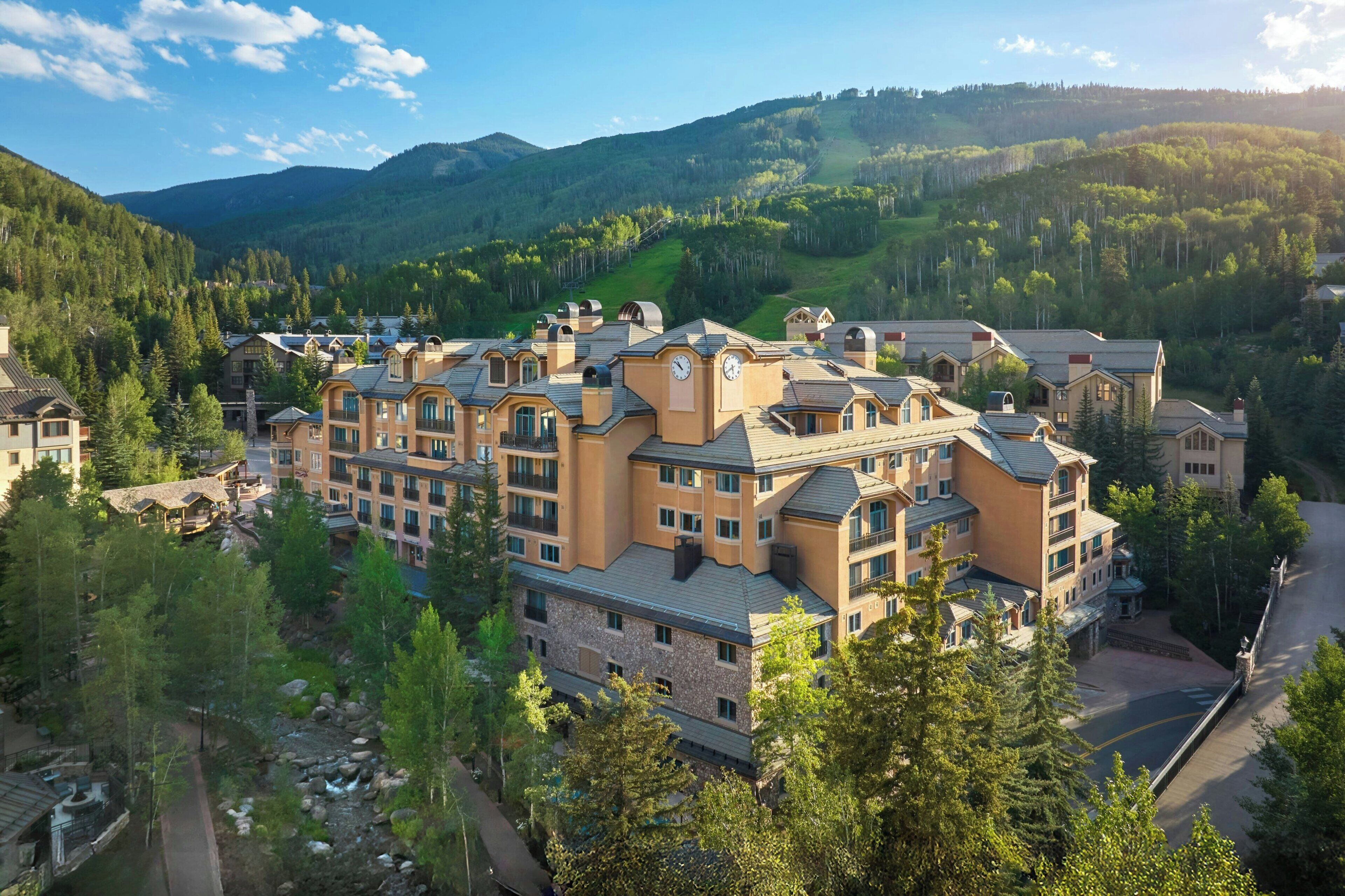 Un hôtel à plusieurs étages doté d’une cour intérieure, entouré d’une végétation luxuriante et avec des montagnes en toile de fond.