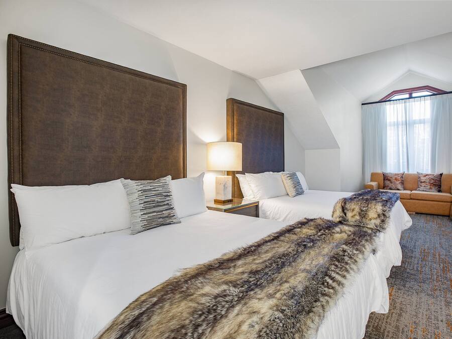 A hotel room with two beds, a sofa, a lamp, and a large window with curtains.