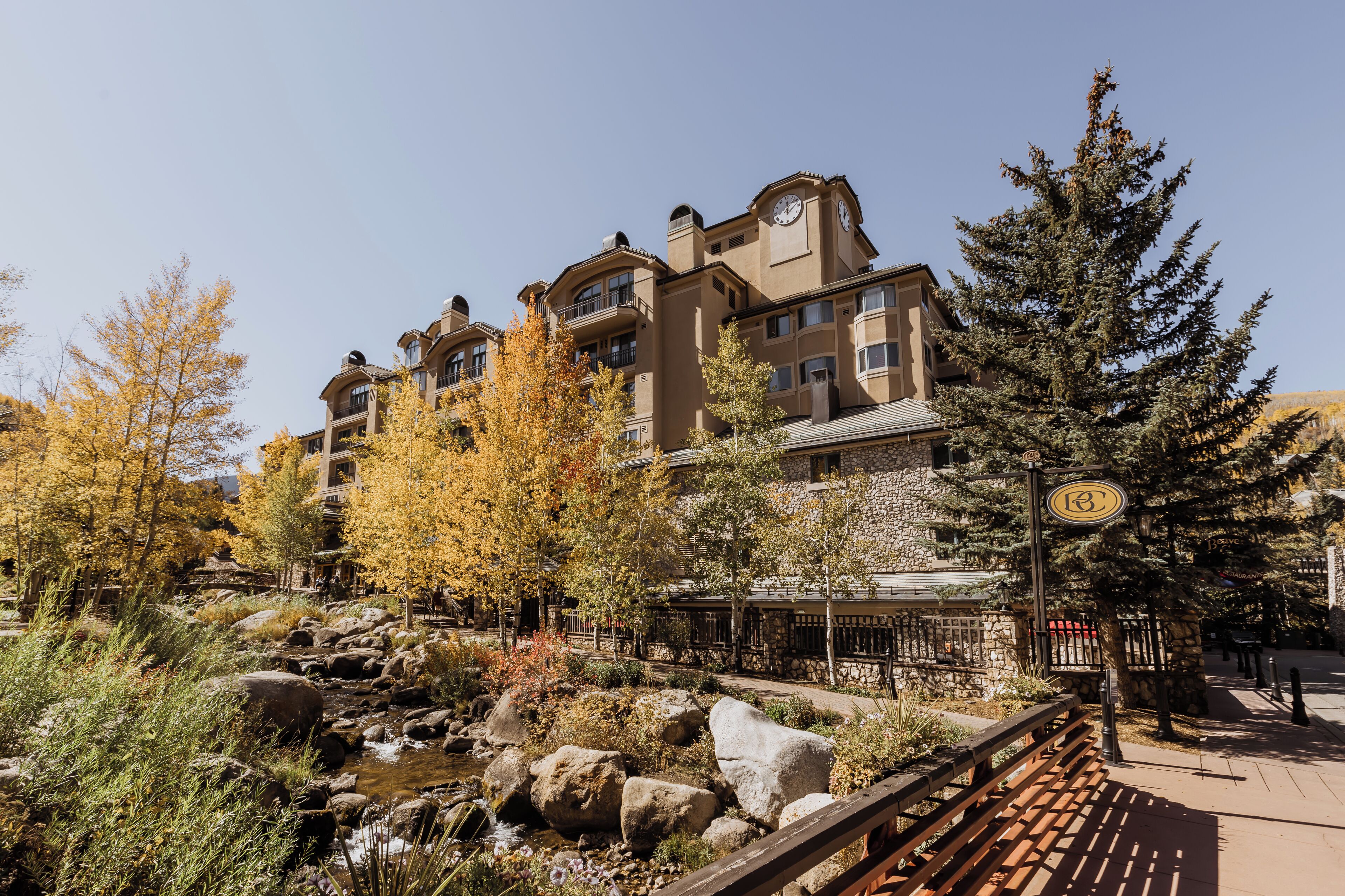 A multi-story hotel with a stone facade, a small stream, and a wooden deck.