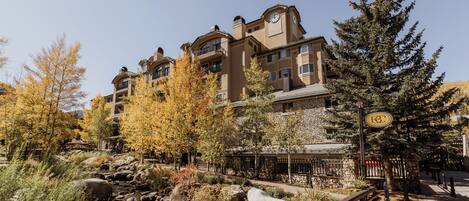 A multi-story hotel with a stone facade, a small stream, and a wooden deck.