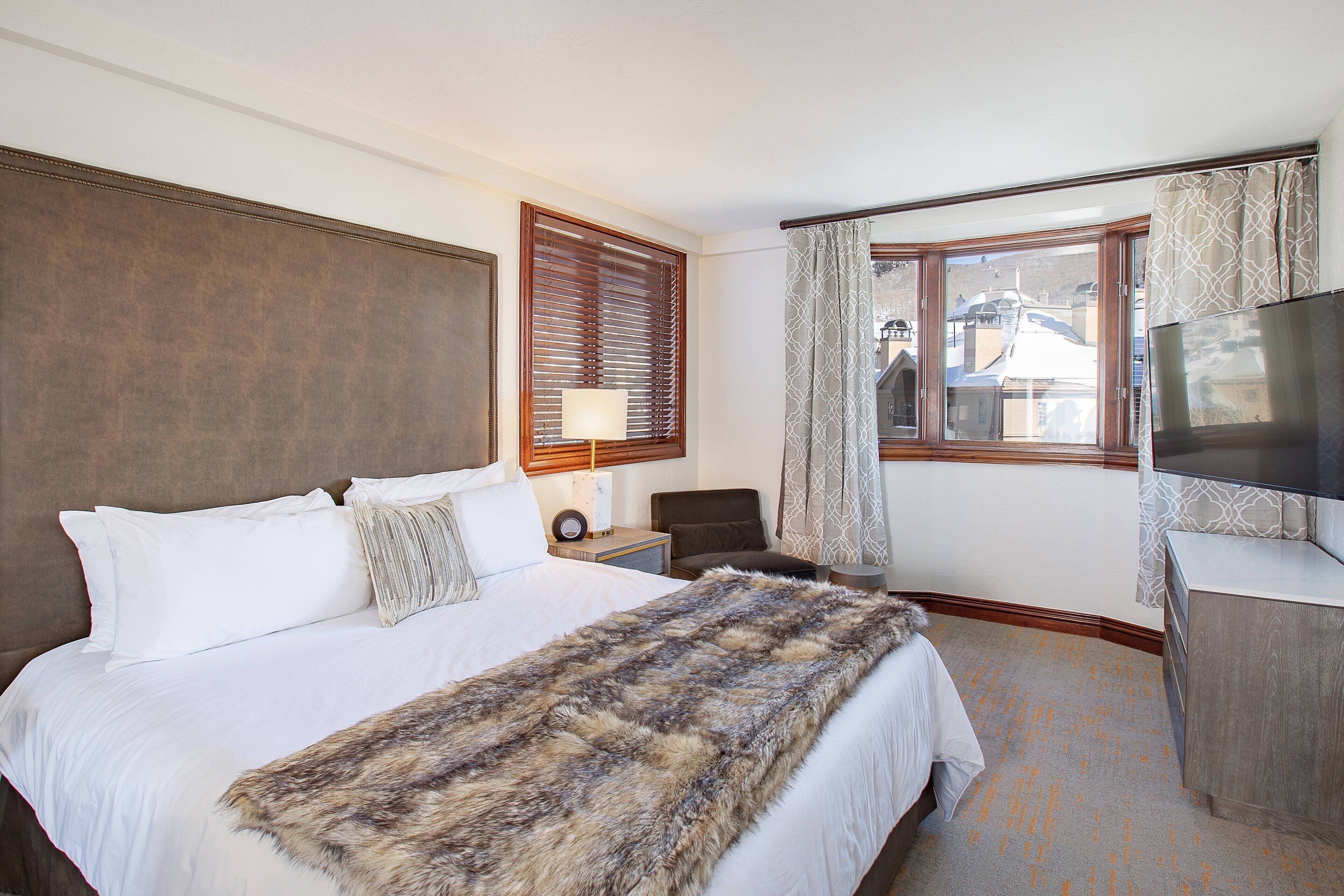 Habitación de hotel con una cama grande, televisión, escritorio y ventana con cortinas.
